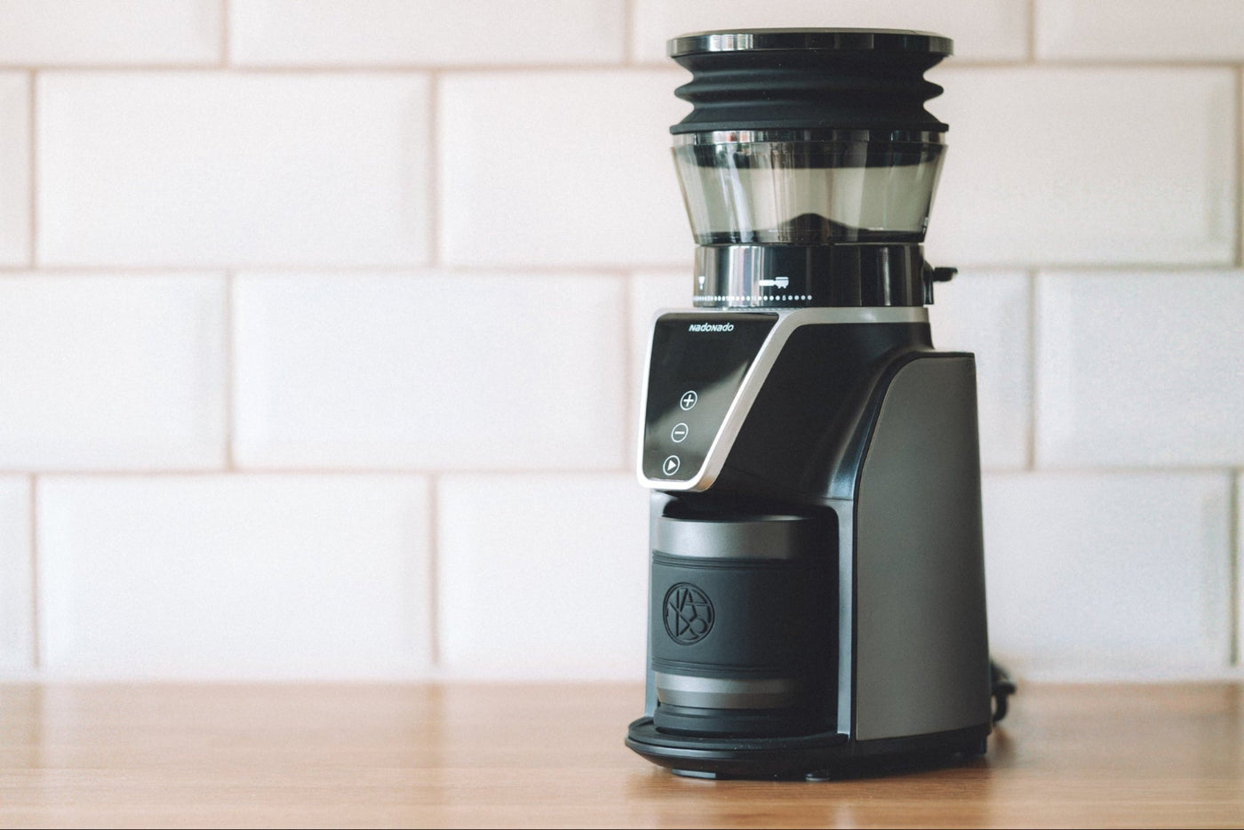 Black coffee grinder on a wooden surface with a white tiled wall background