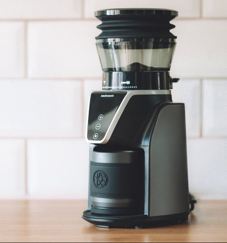 Black coffee grinder on a wooden surface with a white tiled wall background