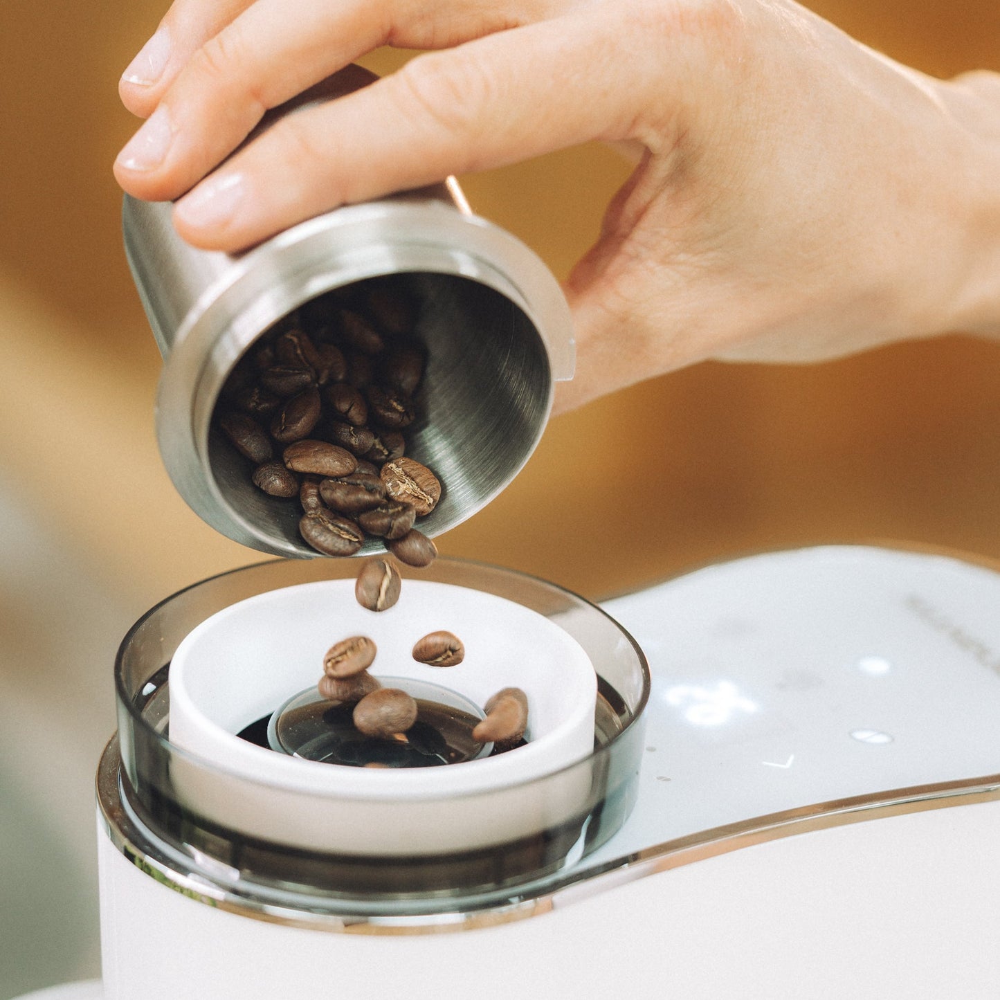Hand pouring coffee beans into a coffee grinder with a blurred background