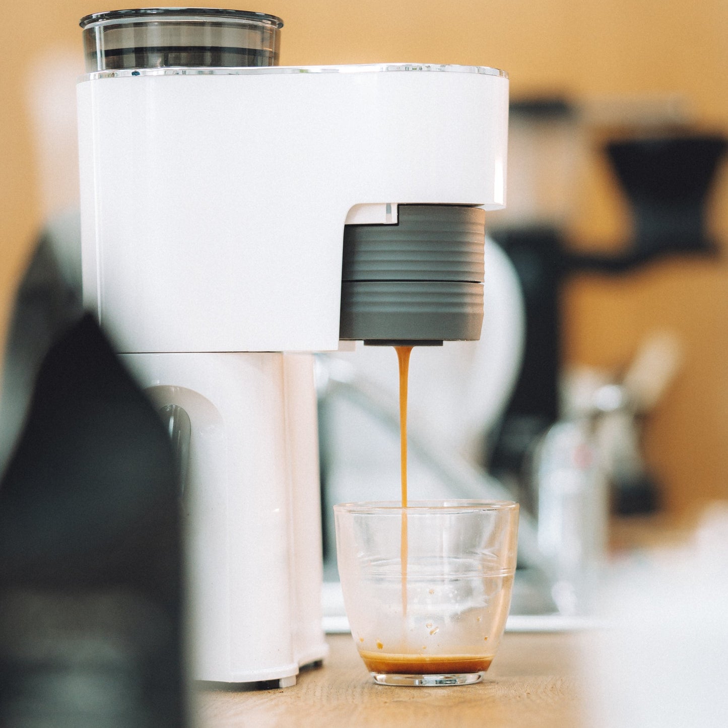 White coffee machine dispensing coffee into a glass on a wooden surface.