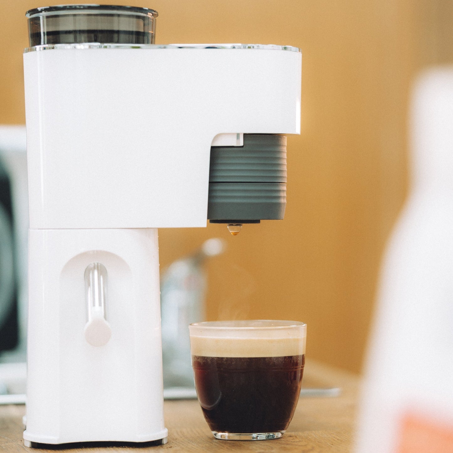 White coffee machine with a glass of coffee on a wooden surface