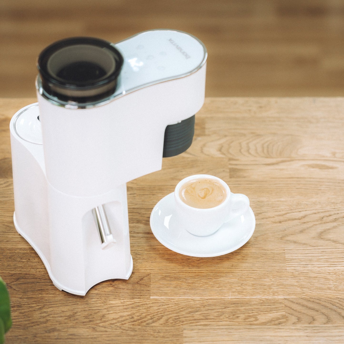 White coffee machine on a wooden table with a cup of coffee next to it