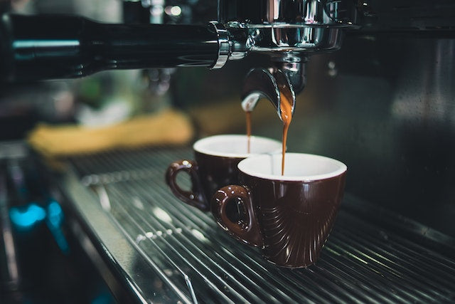 espresso machine pouring coffee into two black espresso cups