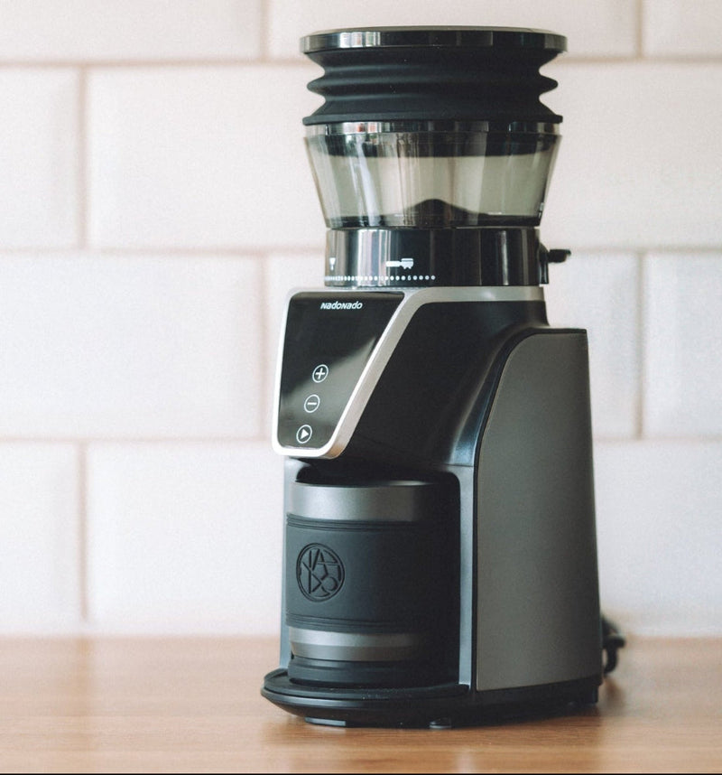 Black coffee grinder on a wooden surface with a white tiled wall background